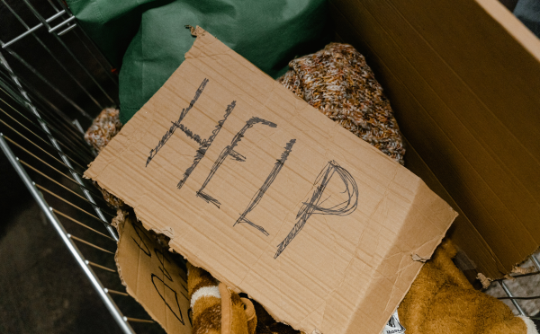A basket with clothing and a cardboard sign reading "HELP"